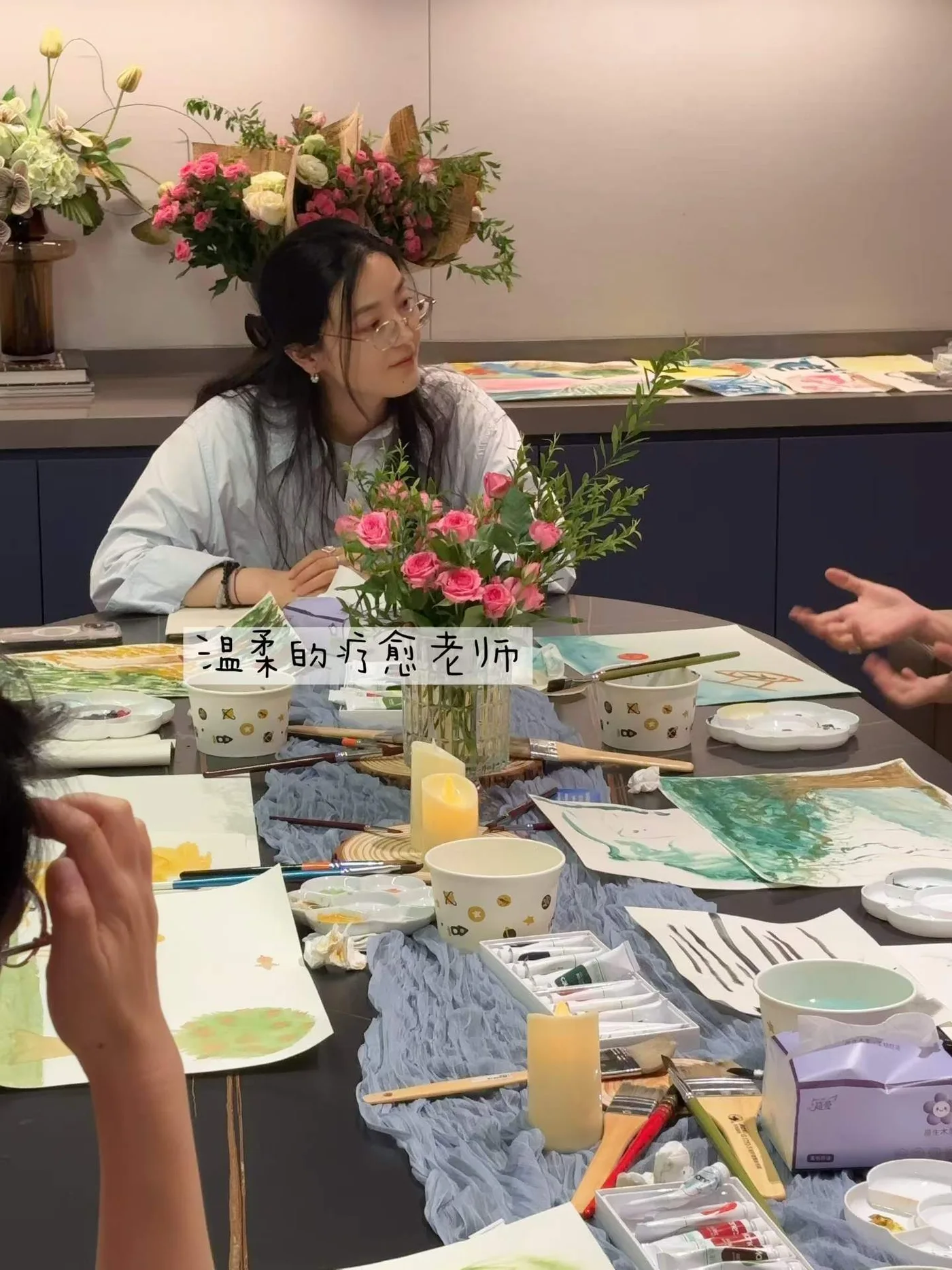 参与者围桌体验绘画活动，桌上放着画纸、画笔和鲜花